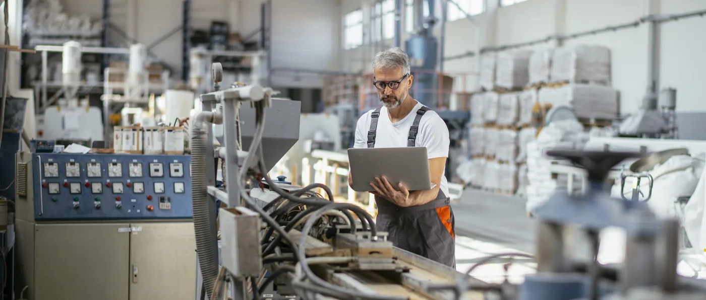 Monteur in overall met een laptop bij een machine in een productiehal