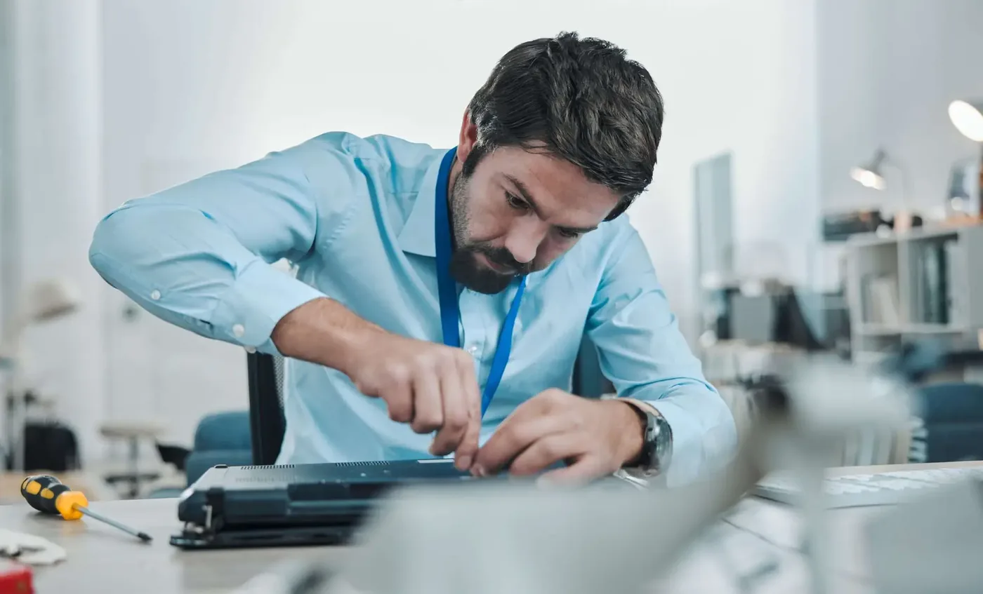 Technicus die aan een geopende laptop werkt, met een schroevendraaier op het bureau
