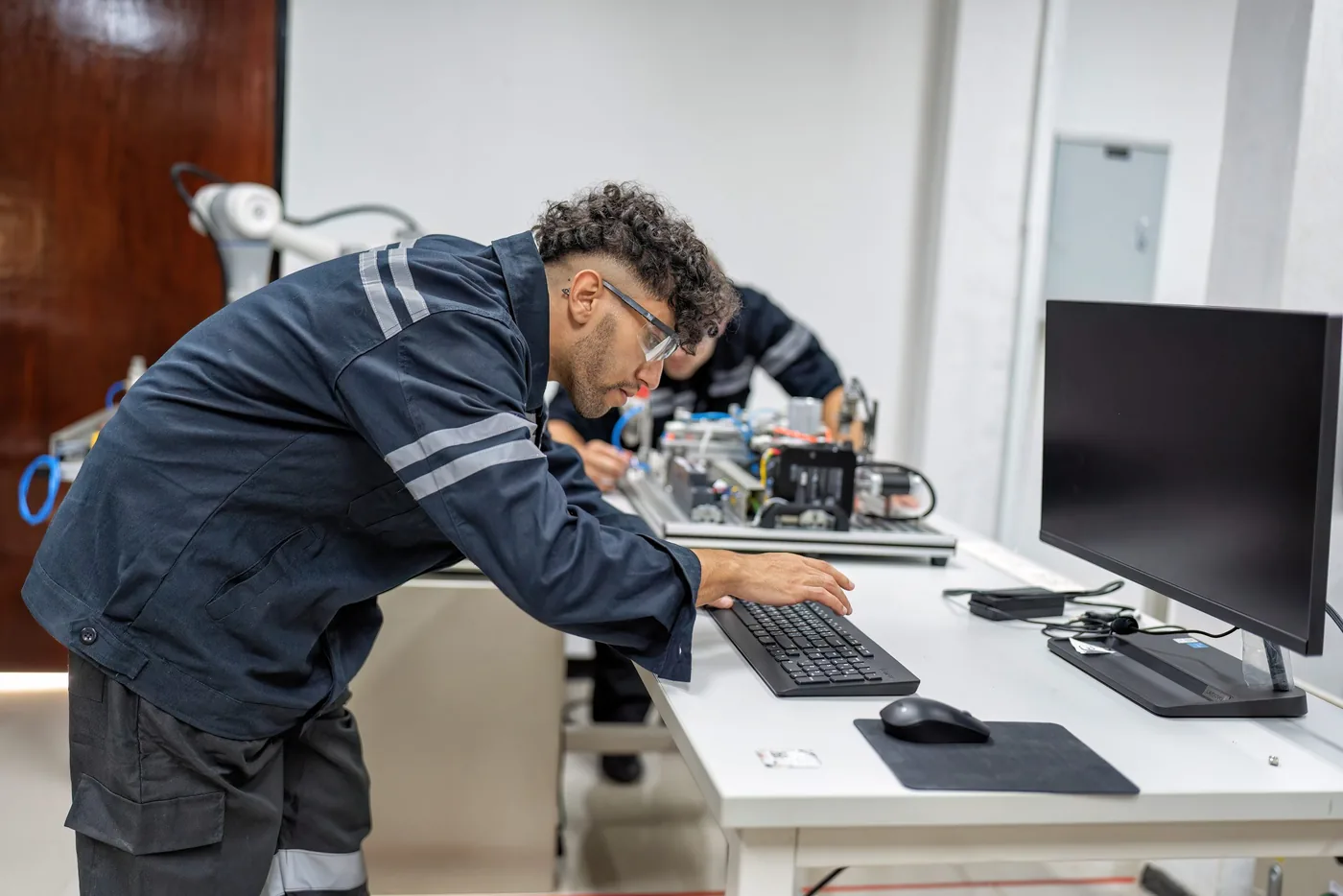 Twee technici in werkkleding aan een witte werkbank met een toetsenbord en meetapparatuur