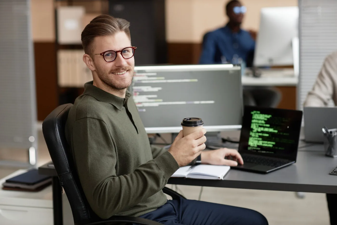 Medewerker met een beker koffie aan een bureau met een scherm vol code