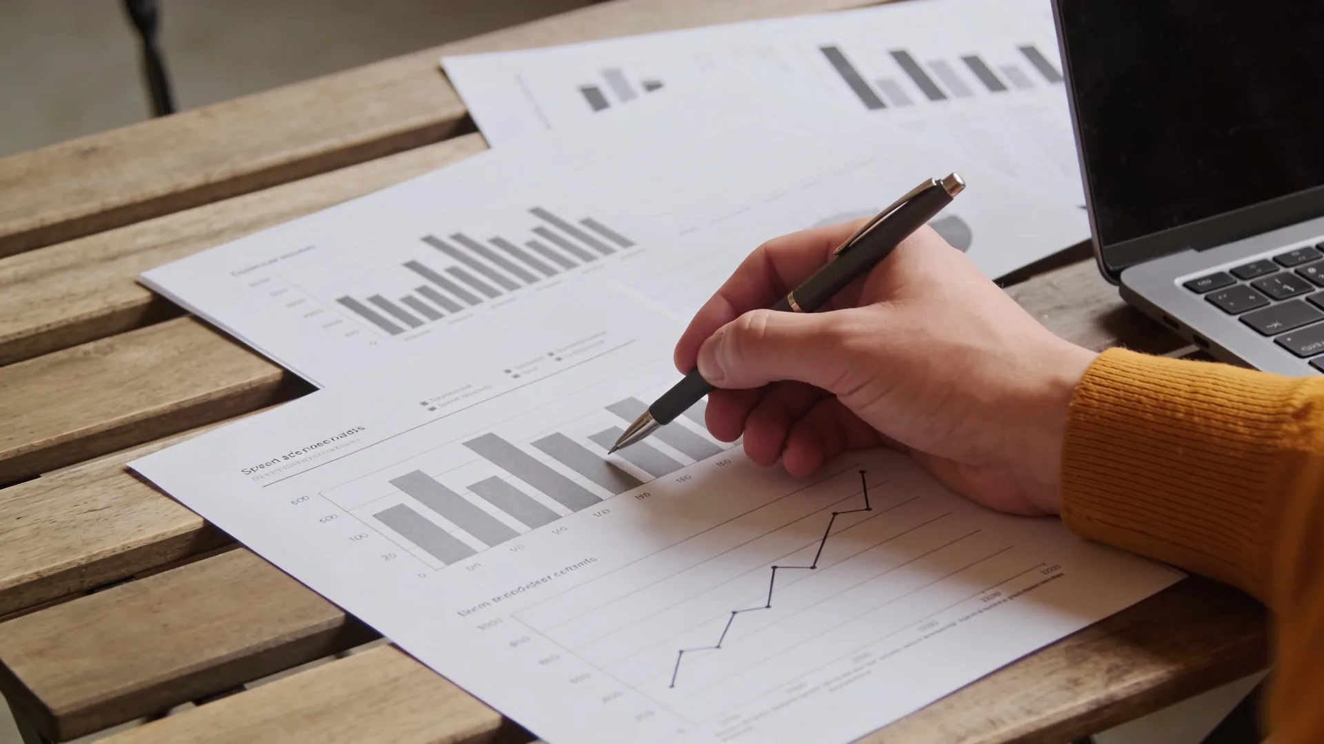 Tafel met uitgeprinte grafieken, een laptop en een hand met een pen